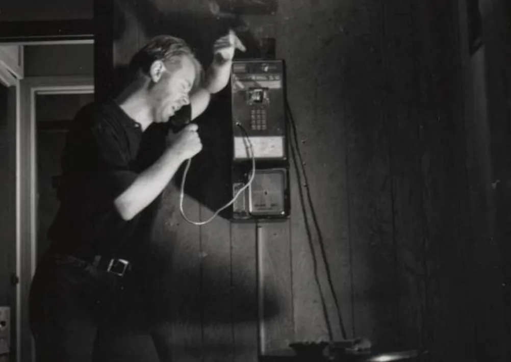 Mark Novak performing beside a payphone in a black-and-white stage photograph