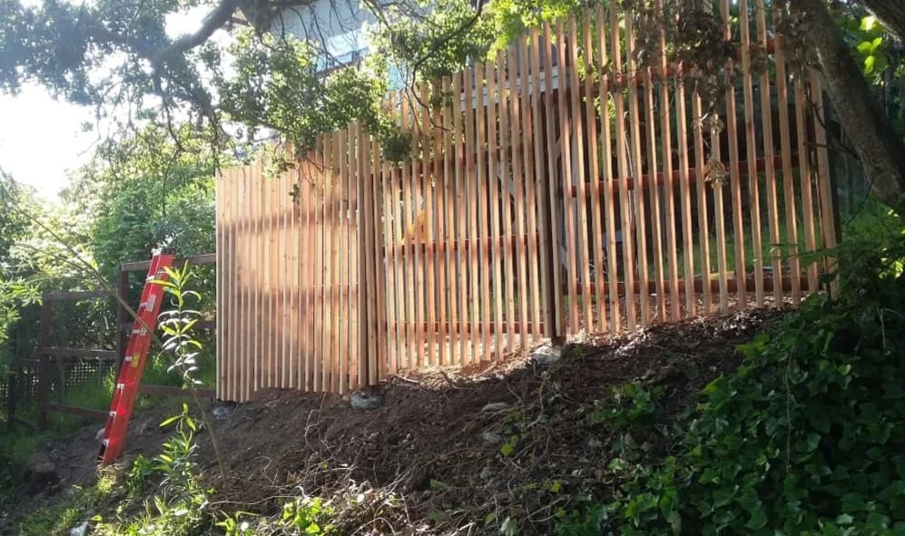 Tall cedar privacy fence under construction on a wooded slope